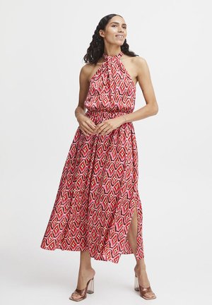 Abito maxi a fantasia rosso e rosa con collo halter, vita elastica e spacchi laterali. La modella indossa sandali trasparenti con tacco.