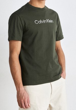 Olivengrøn bomuld T-shirt med korte ærmer og et hvidt "Calvin Klein"-logo i et diskret prikket mønster på tværs af brystet.