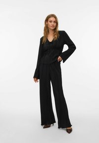 Zwart geplooid tweedelig outfit met een top met lange mouwen en een V-hals en bijpassende wijde broekspijpen. Het materiaal lijkt een textuur te hebben.