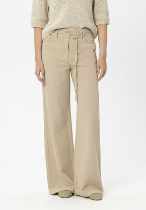 Woman wearing beige wide-leg pants with a matching belt and a beige knit sweater, standing against a plain background.