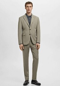 Light gray suit with notch lapels, two buttons, and side pockets. Paired with a dark blue polo shirt and black shoes. Smooth texture.