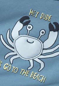 Tessuto blu con un design di un granchio in stile cartone animato, con accenti bianchi e neri, e la scritta "EHI RAGAZZO ANDIAMO IN SPIAGGIA" in giallo.