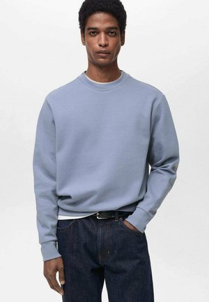 Light blue sweatshirt made of cotton blend fabric. Features a round neckline and ribbed cuffs. Paired with dark denim jeans.