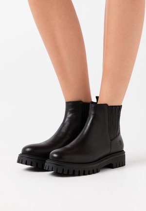 Czarne skórzane botki za kostkę z prążkowanymi elastycznymi panelami po bokach i masywną, ząbkowaną podeszwą. Gładka powierzchnia z minimalnymi detalami i akcentem logo.
