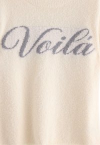 Kreemi neule, jossa on pehmeä ja tekstuuriutunut kudos. Etupuolella on suuri harmaa "Voilà" -grafiikka kursiivilla. Pyöreä pääntie.