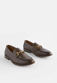 Mocassins en cuir brun foncé avec une finition texturée, dotés d'un accent de quincaillerie décorative en ton or et d'un petit talon empilé.