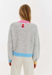 Szary dzianinowy sweter z różowymi, niebieskimi i żółtymi akcentami w prążek przy kołnierzu i dołach. Ma metkę marki z tyłu. Gruba faktura.