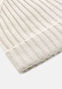 Beige neulottu hattu, jossa on ribbimäinen rakenne, käännetty reuna ja hienot ompelu-yksityiskohdat reunoilla.