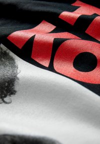 Tela negra con una textura suave que presenta elementos gráficos audaces en rojo y blanco, incluyendo texto y una imagen estilizada en escala de grises.