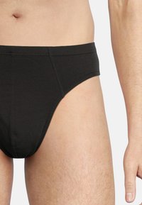 Slip di cotone nero con una texture liscia, design a vita bassa e cintura elastica. Presenta cuciture semplici e un branding minimale.