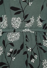 Vihreä kangas, jossa on uritettu pinta, esittelee musta-valkoisia kukkakuosisia kuvioita. Suunnittelussa on lehtiä ja pyöreitä kukkaaksentteja, luoden toistuvan motiivin.