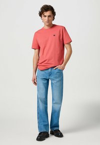 Korallfärgad bomull T-shirt med korta ärmar och rund halsringning, tillsammans med ljusblå rakben jeans och svarta skor.