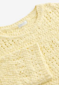 Pull en maille couleur crème avec un motif texturé, un col rond et une étiquette de marque visible à l'intérieur du col.