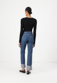 Black long-sleeve shirt, high-waisted blue denim jeans with light blue cuffs, and black shoes with button accents, viewed from the back.