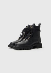 Bottes cheville en cuir noir avec un bout arrondi, des œillets dorés, des lacets noirs et une semelle en caoutchouc épaisse et texturée.
