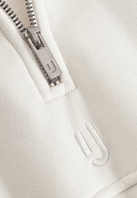 White zip-up sweatshirt featuring a silver zipper and subtle embroidered logo. Smooth texture with a fitted design.
