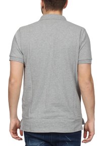 Šedé polo tričko s krátkým rukávem a límečkem, hladkým povrchem a bočními rozparky na dolním lemu. Materiál má jednoduchý, jednobarevný design.