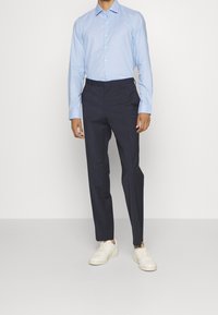 Lichtblauwe overhemd met lange mouwen gecombineerd met donkerblauwe broek en witte sneakers. Het overhemd heeft een button-down kraag en manchet.