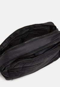 Borsa nera imbottita con più scomparti con zip e una texture in tessuto liscia, caratterizzata da un design minimalista e dettagli di cucitura orizzontale.