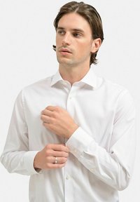 Hvid langærmet skjorte med knapper lavet af bomuld. Har en klassisk krave, enknapsmanchetter og en glat tekstur med minimal dekoration.