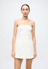 Strapless white dress with textured floral appliqué, fitted silhouette, and frayed hem. Smooth fabric with a structured design.