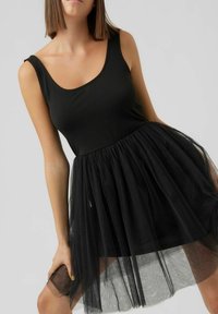 Schwarzes ärmelloses Kleid mit einem taillierten Oberteil und einem mehrlagigen Tüllrock, mit einem transparenten Stoff und sanften Raffungen an der Taille.