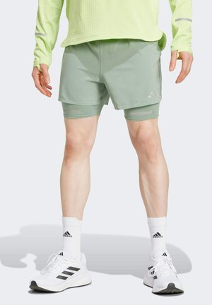 Shorts deportivos de color verde claro con un diseño texturizado, presentando un look en capas. Combinados con zapatillas blancas y calcetines de marca.