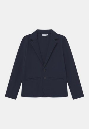 Blazer bleu marine sur mesure avec revers crantés, deux boutons à l'avant et deux poches passepoilées horizontales.