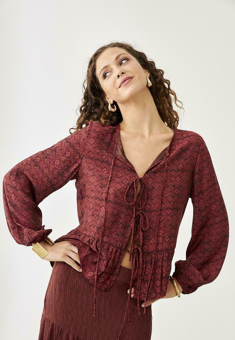 Blusa floral burdeos con mangas largas, detalle de lazo en el frente y dobladillo con volantes. Tejido ligero con una textura sutil.
