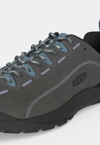 Basket KEEN grise et bleue avec des lacets à motifs, des coutures visibles et une semelle en caoutchouc noire sur fond blanc.