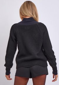 Schwarzer Strickpullover mit einem gerippten hohen Kragen, lockerer Passform und überschnittenen Schultern. Verfügt über ein strukturiertes Muster und einen abgerundeten Saum.