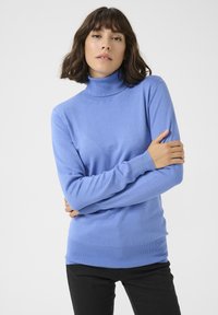 Jasnoniebieski sweter typu golf wyk wykonany z miękkiej dzianiny, z długimi rękawami oraz ściągaczami przy mankietach i u dołu, noszony z czarnymi spodniami.