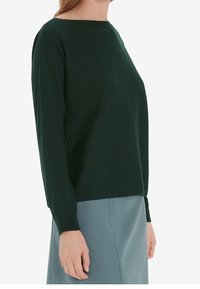 Maglione verde scuro in tessuto morbido, con colletto rotondo e maniche lunghe, abbinato a una gonna azzurro chiaro. Texture liscia, senza motivi.