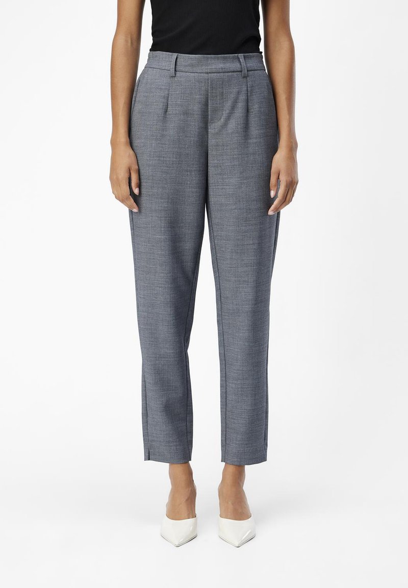 Grau maßgeschneiderte Hose mit strukturiertem Finish, hoher Taille, seitlichen Taschen und schmalen, verkürzten Beinen. Weiße spitz zulaufende Absätze runden das Outfit ab.