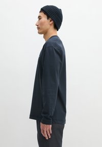 Navyblaues Langarmshirt aus weicher Baumwolle mit schlichtem Design und Rundhalsausschnitt. Kombiniert mit dunkelgrauer Hose und einem gerippten Beanie.