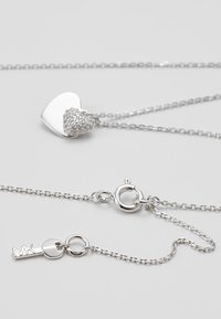 Collier en chaîne d'argent avec un pendentif en forme de cœur, partiellement lisse et partiellement incrusté de petits cristaux, avec une fermeture à ressort.