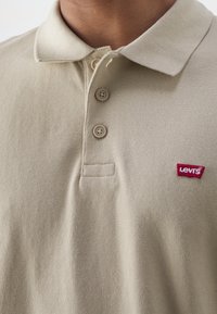 Béžová polo košile Levi's s texturovanou tkaninou, třemi knoflíky a malým červeným logem na hrudi. Klasický design límce.
