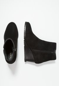 Bottines en daim noir avec talon compensé, dotées d'une fermeture éclair latérale et d'une finition lisse et texturée. Design compact avec une silhouette courbée.