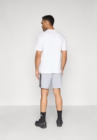 Conjunto para hombre que incluye una camiseta blanca lisa, pantalones cortos grises con rayas negras a los lados, zapatos negros y calcetines oscuros, visto desde atrás.