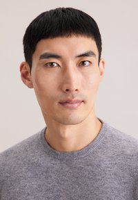 Grauer Pullover mit texturierter Oberfläche, rundem Ausschnitt und geripptem Kragen; Nahaufnahme eines Mannes mit kurzen, dunklen Haaren und neutralem Ausdruck.