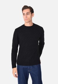 Maglione nero lavorato a maglia con motivo esagonale, scollo rotondo e polsini a coste, abbinato a jeans in denim blu.