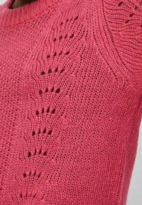 Maglione rosa lavorato a maglia con un motivo testurizzato e punti aperti lungo l'area delle spalle e un colletto rotondo.