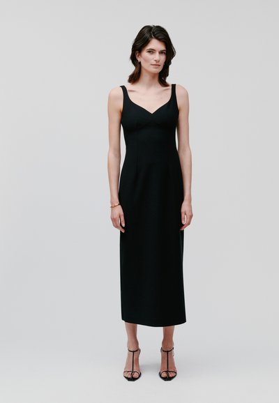 Black sleeveless midi dress with a sweetheart neckline and fitted silhouette. Smooth texture, minimal design, no patterns. Stiletto heels.