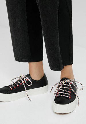 Baskets en cuir noir avec semelles plates-formes blanches, dotées de lacets multicolores rayés et d'un design à bout rond.