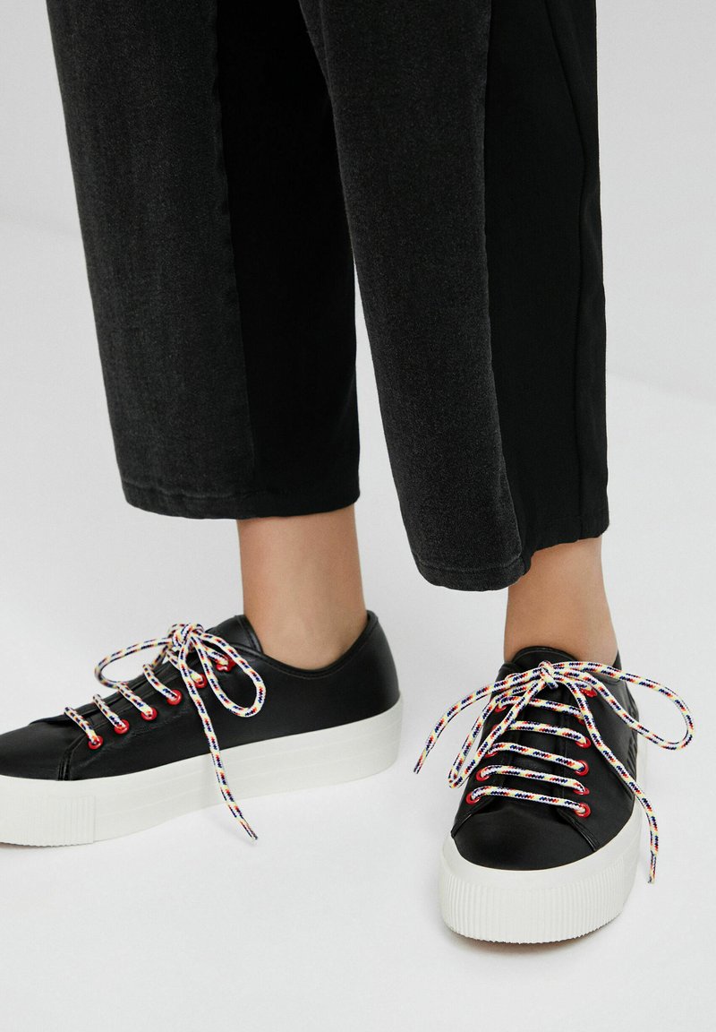Baskets en cuir noir avec semelles plates-formes blanches, dotées de lacets multicolores rayés et d'un design à bout rond.