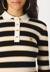 Černé a krémové pruhované polo tričko s texturovanou vazbou, zdobené zlatými akcenty, s pěti knoflíky a logem na hrudi.