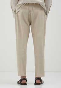 Beige Hosen mit geradem Schnitt, aus einem glatten Stoff, mit zwei Gesäßtaschen, getragen mit schwarzen Sandalen.