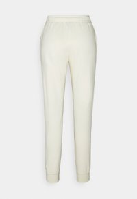 Calças de treino cor creme com cintura elástica, tornozelos ajustados e textura suave. Projetadas para conforto e uso casual.