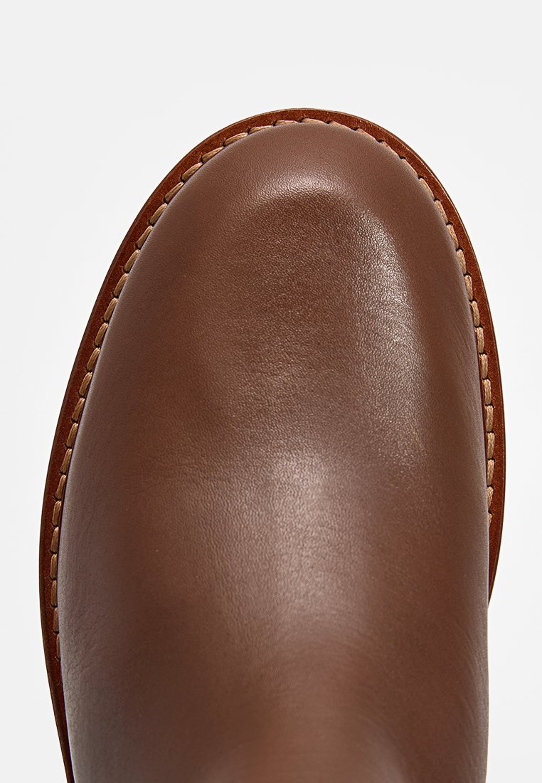 Braune Lederstiefel mit glatter Oberfläche, runder Zehenform und sichtbaren Stichdetails entlang der Kante.