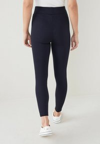 Granatowe legginsy z wysokim stanem, dopasowane, elastyczny materiał, bez widocznych wzorów; w połączeniu z białymi butami na slip-on.